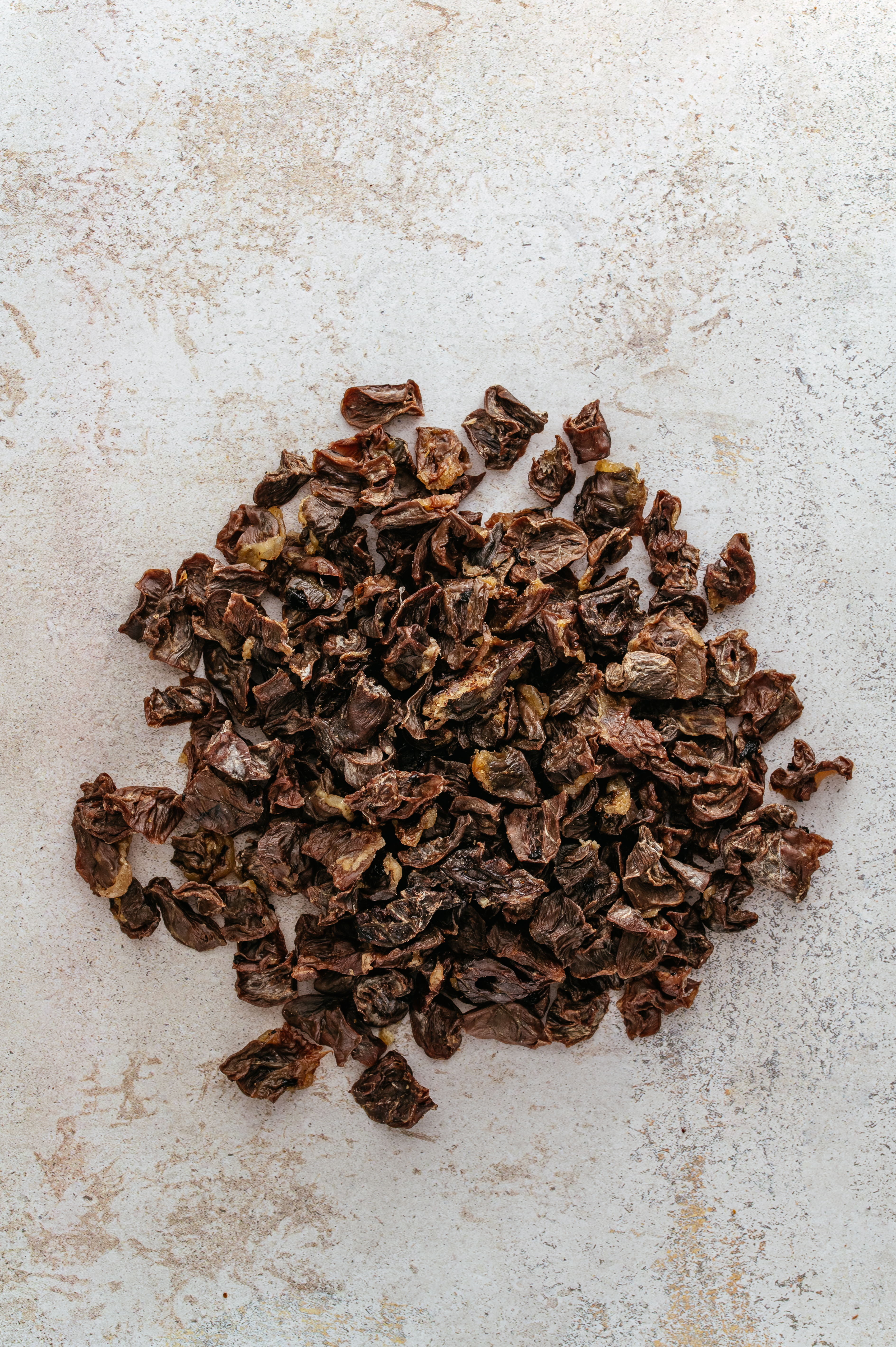 Vue de dessus d'un tas de cascara (enveloppes de cerises de café séchées) aux éclats brun foncé, disposé au centre d'un fond en pierre claire et texturée.